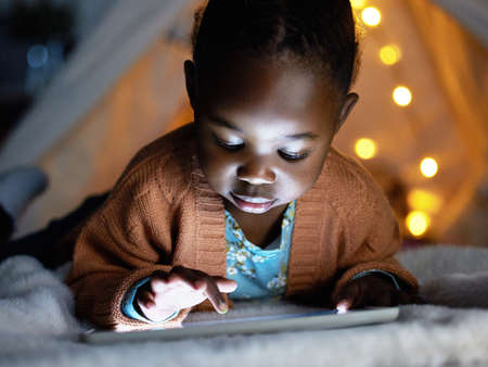 A small device packed with big life lessons. an adorable little girl using a digital tablet during bedtime at home.の写真素材