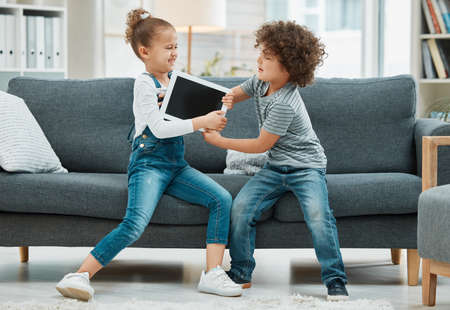 But its my turn. two siblings fighting in a game of tug of war over their digital tablet.の写真素材