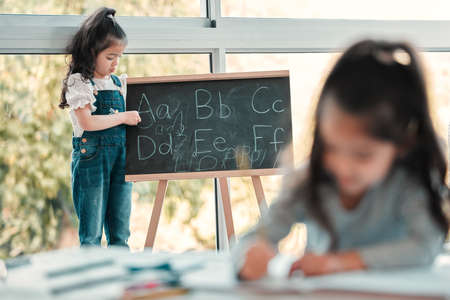 Lets rearrange the alphabet. a young girl writing on a blackboard.の写真素材