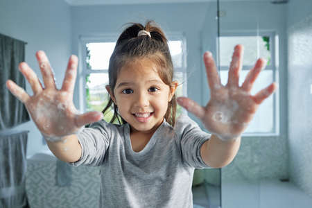 Look at how well Im washing them. Portrait of an adorable little girl holding up her soapy hands in a bathroom at home.の写真素材