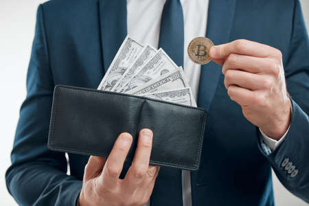 Money comes in different forms. Closeup shot of an unrecognisable businessman holding a bitcoin and a wallet filled with banknotes against a white background.の写真素材