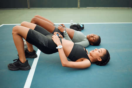 Working on their core. Full length shot of two attractive young female athletes doing hip raises while exercising outdoors on a sports court.の写真素材