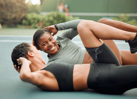 Motivation is right by your side. two attractive young female athletes doing leg raises during their workout on a sports court.の写真素材