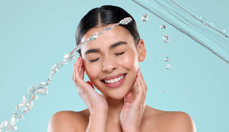 Feeling fresh and feminine. a beautiful young woman being splashed with water against a studio background.の写真素材