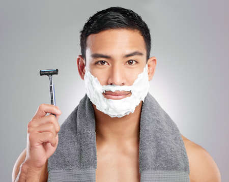 Its between me and my beard. Studio shot of a handsome young man shaving against a grey background.