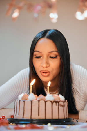 I hope all my wishes come true. a young woman blowing candles on a cake while celebrating her birthday at home.の写真素材