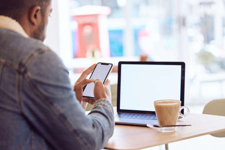 Never going back to an office. a man using his smartphone and laptop to work in a coffee shop while...