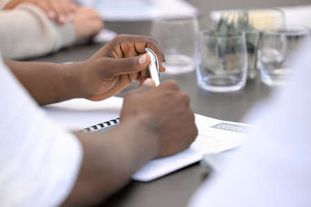 Sitting down with the annual report. Closeup shot of an unrecognisable businessman going through paperwork during a meeting in an office.の写真素材