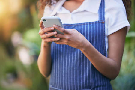 Happy to do it for you. a business owner using her smartphone to send a text.の写真素材