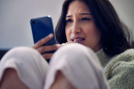 Help is a hello away. a young woman using a smartphone and looking unhappy at home.