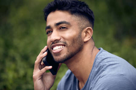 The guy everyone loves to get a call from. a young man using a smartphone while taking a break in a park.の写真素材