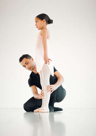 Ballet teaches kids discipline and focus. a ballet teacher assisting a student with her position in a dance studio.の写真素材