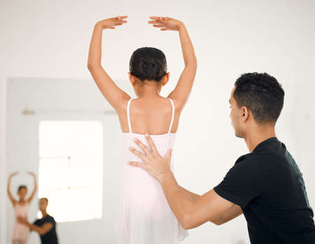Stand up straight and lift your arms up. a ballet teacher assisting a student with her position in a...
