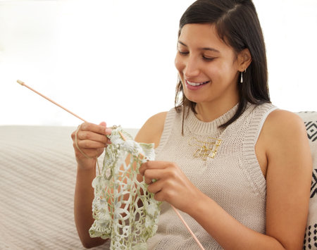Being creative brings me joy. a young woman knitting while relaxing on a sofa at home.の写真素材