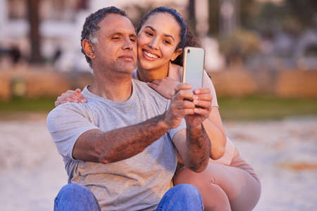She taught me how to take selfies. a mature man using a cellphone to take selfies with his daughter during a day on the beach.の写真素材