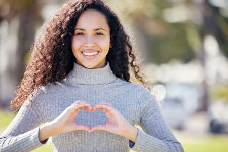 Ive got nothing but love for this world. an attractive young woman standing alone outside making a heart-shaped gesture.の写真素材