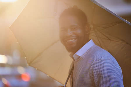 Look forward to the rainbow after the rain. Portrait of a young man holding an umbrella on a rainy day in the city.の写真素材