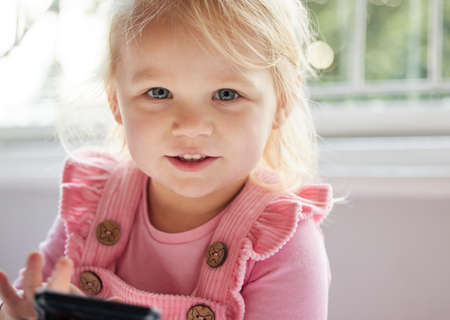 Can I play games. a little girl using a phone at home.