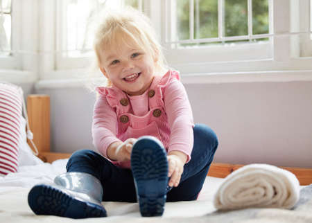 Putting on my best boots. a little girl putting on her boots at home.の写真素材