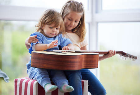 She loves teaching her sister something new. two little sisters playing the guitar at home.の写真素材
