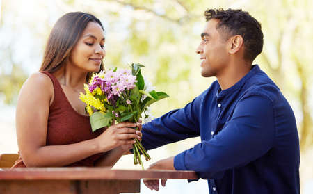 Making their date as romantic as possible. a handsome young man giving his girlfriend flowers during their date on a wine farm.の写真素材