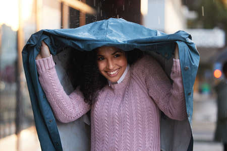 Its a day to be covered up. a young woman covering herself with a coat in the rain in the city.