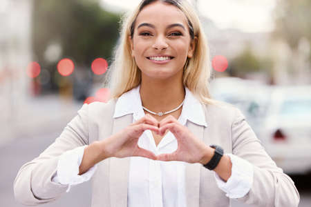 Spread love. Cropped portrait of an attractive young businesswoman making a heart shape with her hands while walking through the city.の写真素材
