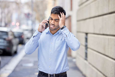 I cant get fired. a handsome young businessman walking through the city and feeling stressed while using his cellphone.の写真素材