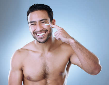 Master of one. Studio portrait of a young man happily applying moisturiser to his face against a grey background.の写真素材