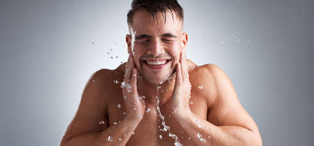 Studio shot of a handsome young man washing his face against a grey background.の写真素材