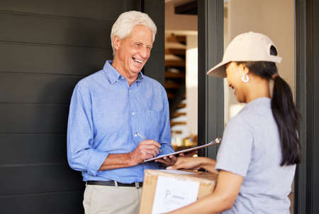 Just sign right there. a handsome senior man taking delivery of a package from a female courier.の写真素材