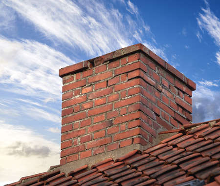 Closeup of red brick chimney chute against blue sky with clouds for combustion gas or home...