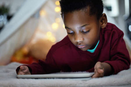 How late is too late. an adorable little boy using a digital tablet during bedtime at home.