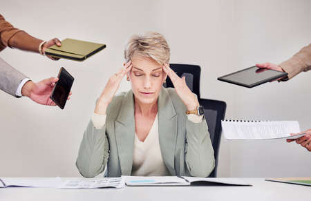 The joys of being their manager. a mature businesswoman sitting in the office and feeling stressed while her colleagues put pressure on her.の写真素材