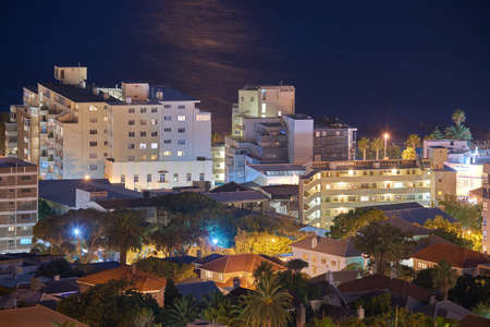 Night cityscape view of city buildings with electricity lights, infrastructure and sea or ocean...