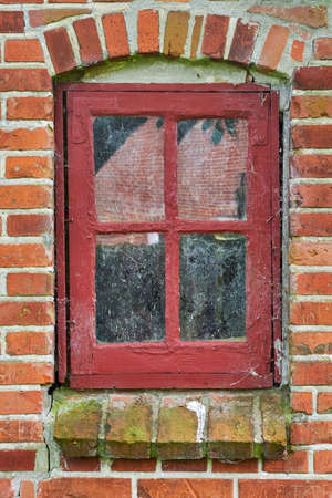 Closeup of abandoned red window covered in spiderwebs, algae and moss from neglect, poverty and economic crisis. Empty, old residential building or home in a village with damp mold on the windowsillの写真素材