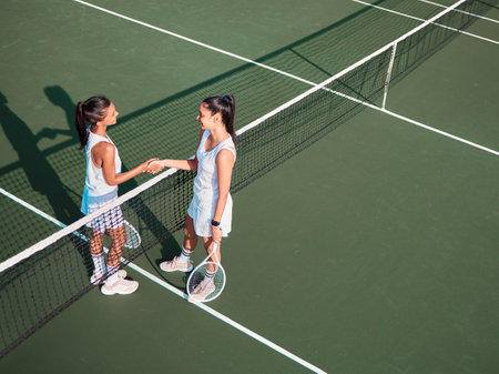 I enjoyed having you as my opponent. two sporty young women shaking hands while playing tennis together on a court.の写真素材