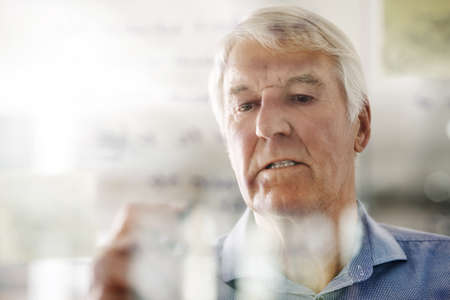 a senior businessman writing down ideas with a pen marker on a glass wall in the office.