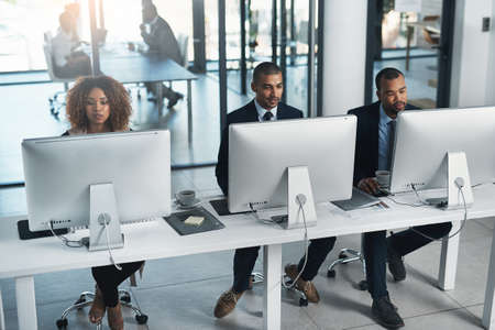 High angle shot of three corporate businesspeople working on their computers in the office.の写真素材