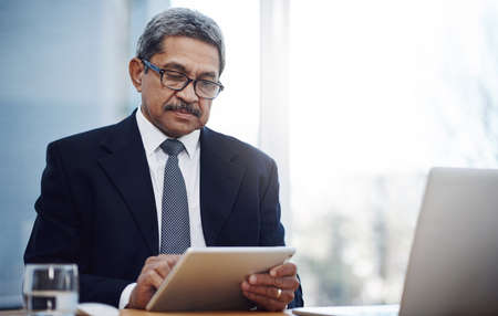 He never fails to make all the smart moves in business. a mature businessman working on a digital tablet in an office.の写真素材