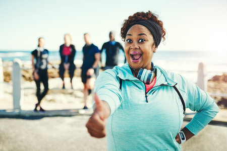 Youd be just as surprised by the benefits of exercising. Portrait of a sporty young woman showing thumbs up while exercising outdoors.の写真素材