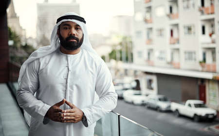 Taking a break on the balcony. Cropped portrait of a businessman dressed in traditional Islamic clothing working on his office balcony.の写真素材