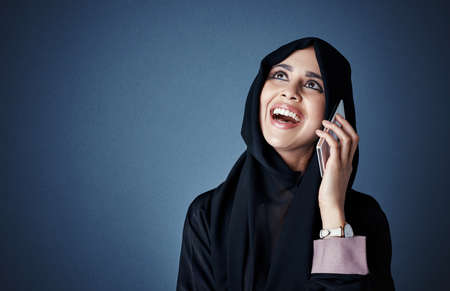 Thats great news. an attractive young businesswoman making a call while standing against a dark background.の写真素材