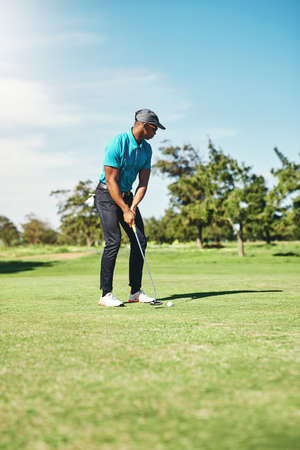 Gently now. a focused young male golfer about to play a shot with his putter on a golf course outside during the day.の写真素材