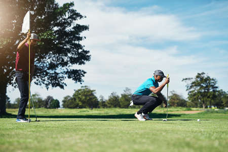 This one is going to be in. a focused young male golfer looking at a golf ball while being seated on the grass outside during the day.の写真素材