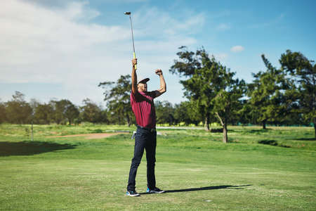 What a shot. a cheerful young male golfer lifting up his hands in success of playing a good shot outside during the day.の写真素材