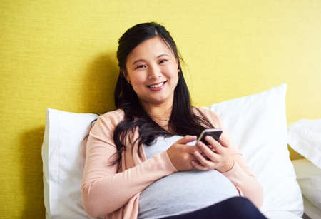 Got to keep in touch with loved ones about my pregnancy. Portrait of a pregnant woman using a...