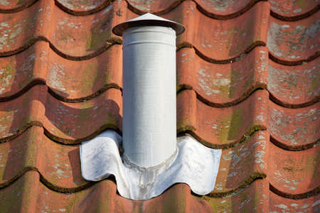 Closeup shot of a white steel chimney on an old brown tile roof outside. Stay warm this winter with...