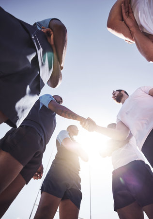 Below two opponent rugby teams shaking hands before or after a match outside on a field. Rugby players sharing a handshake to show respect and sportsmanship. A mutual understanding of the gameの写真素材