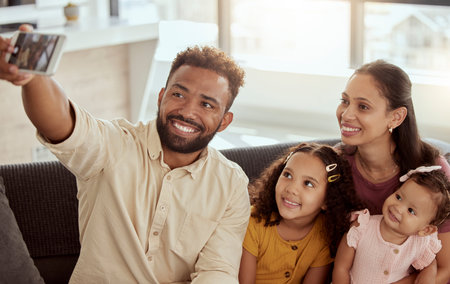 Smiling mixed race parents taking selfie on cellphone with adorable daughters. Happy hispanic man...